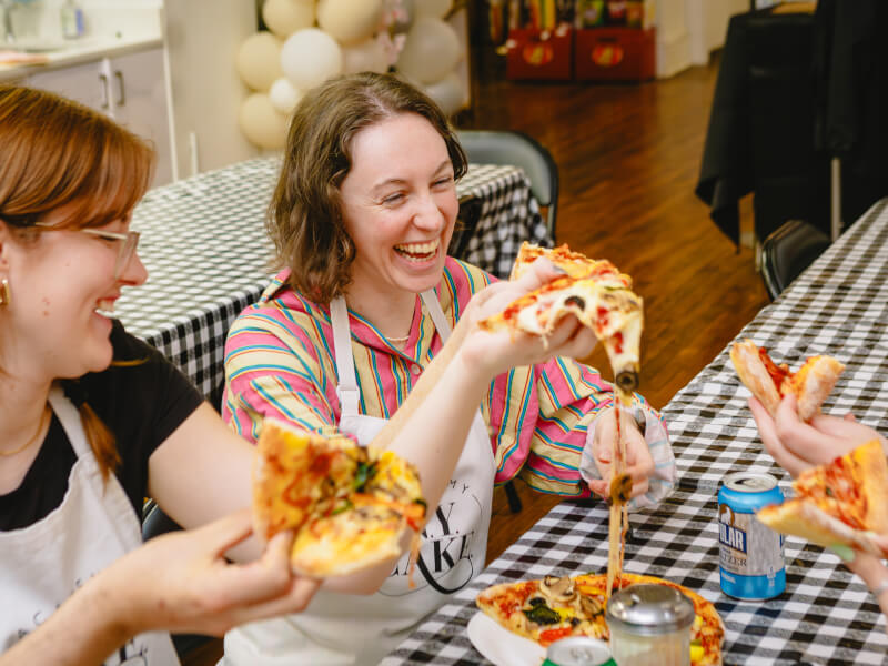 A group of people smiling and laughing as they enjoy a pizza together